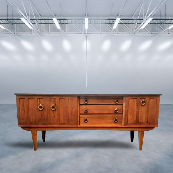 Mid-Century UK Modern Southeast Asian crown-cut new-growth teak credenza with a strip of African Afrormosia wood across the top edge.

Hanging wooden ring pulls open the drawers and cabinets.

Credenza features a two-door cabinet on the left fitted with one removable shelf; three storage drawers in the middle; and a fall-front cocktail cabinet on the right.

Manufactured in England by Beautility.
