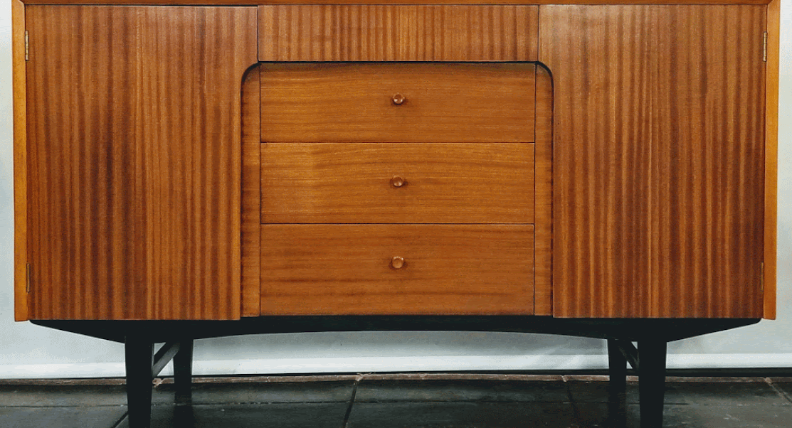 Mid-Century UK Modern credenza by The Co-Operative Wholesale Society has shelved single-door cabinets on each side and four drawers at center. The oak carcase is veneered with ribbon cut Sapele wood from Africa. The trim and knobs are Birch wood.