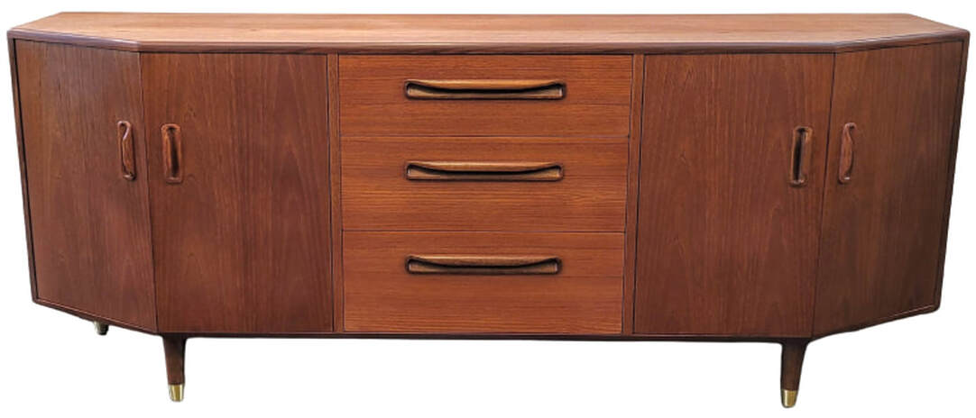 The Fresco canted credenza debuted G-Plan's New Models Folder of 1980. This buffet base could be paired at the time with an optional buffet top designed for the unit. Many Fresco Range pieces were designed by Victor Bramwell ( V.B. ) Wilkins. The credenza is fitted with double-doored canted cabinets to the left and right and three storage drawers down the center. The top drawer is fitted with spacers and lined for flatware storage. The credenza is veneered with Southeast Asian Crown Cut New Growth Teak. The trim and inset pulls are of African Afrormosia wood.