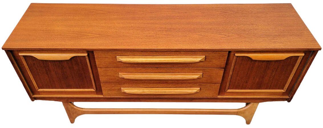 Vintage credenza from England is from Stonehill Furniture's Danish Modern influenced Stateroom range. Credenza is constructed teak veneers and birch wood solids. The top features a beautiful cut of Southeast Asian crown-cut teak. The door and drawer pulls, front trestle base, side stretchers, and door panel framing are birch wood. Credenza has one single door cabinet on each front end and three stacked drawers in the center. The cabinets are lined with mottled sapeli wood from Africa and each cabinet contains one removeable sapeli wood shelf. 63.5