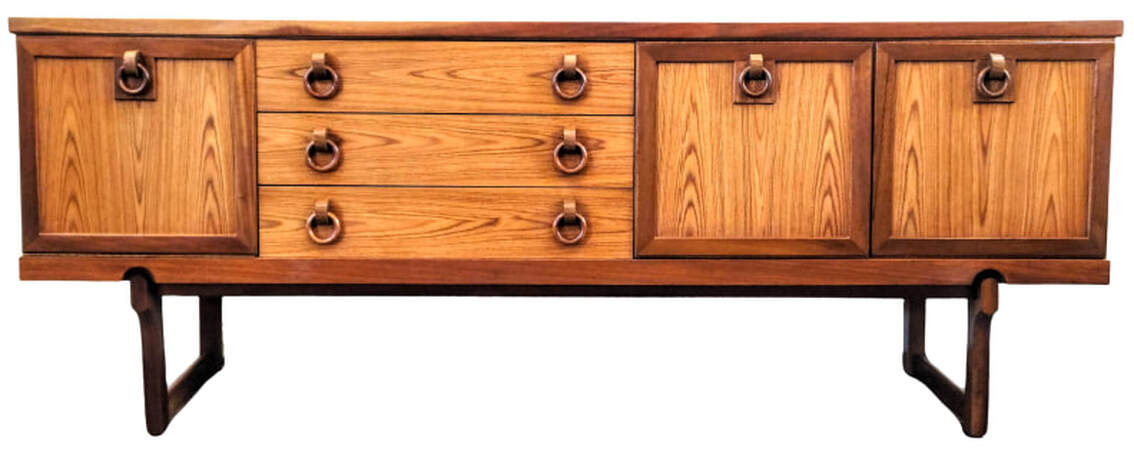 Beautility vintage credenza from England is finished with new growth crown-cut Southeast Asian teak veneers and mahogany wood solids. The front of the credenza offers access to a fall-front cocktail cabinet on the left, three stacked storage drawers at left center, and a two door cabinet fitted with one shelf on the right. The drawers and cabinet doors feature wooden drop ring pulls often applied by Beautility to their Mid-Century Modern credenzas. The door panel frames, trim, and sled legs are in mahogany wood. The cabinet interiors are lined with mottled sapeli wood from Africa. 72.25