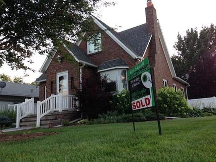 Color photo of older brick house with a sold sign in the front yard.