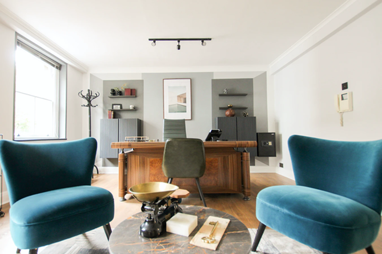 Gian Paolo Aliatis working space interior showing two blue velvet upholstered chairs at the sides of a round cocktail table with desk in background.