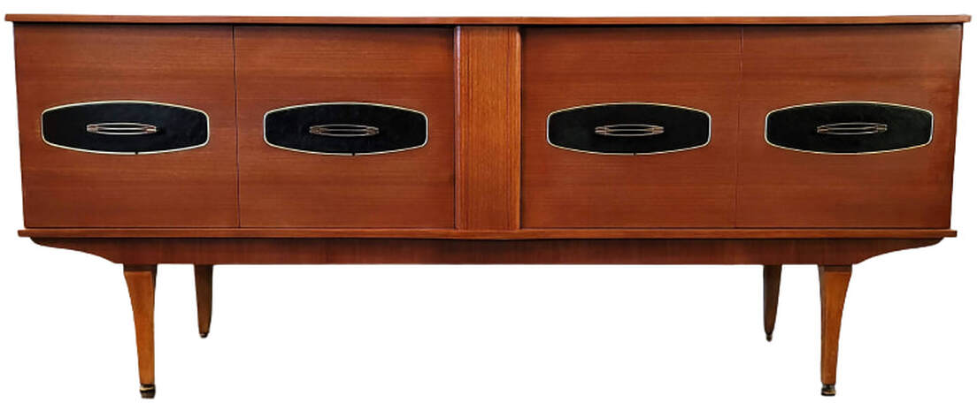 Stonehill Furniture teak credenza from the Danish Modern influenced Stateroom Range.  Teak credenza has bifold doors fronted with rounded rectangle brass trim framed faux black leather panels with pierced pulls.  The carcase stands atop an apron with curved ends and tapered legs.