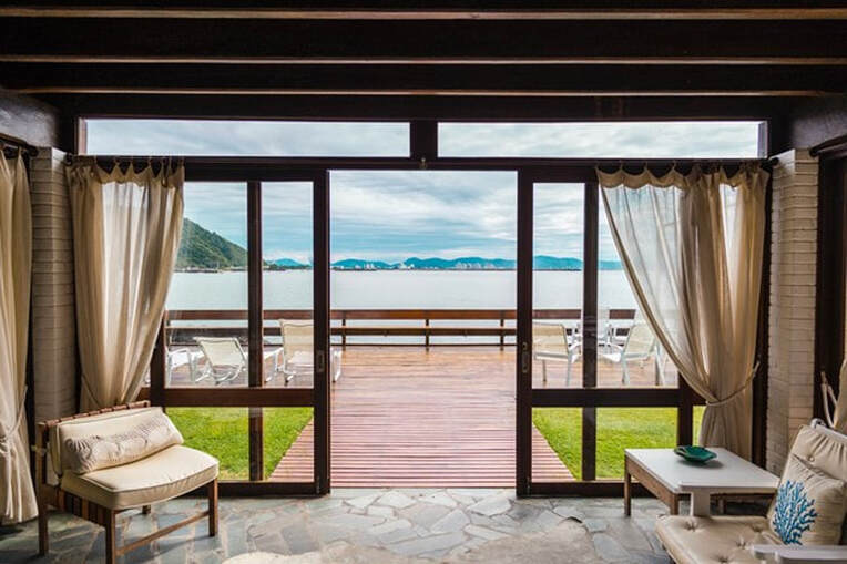 View of sailboats on the water from sliding glass doors looking out to a wooden deck.