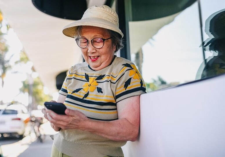 Elderly woman wearing glasses and smiling while looking at cell phone.