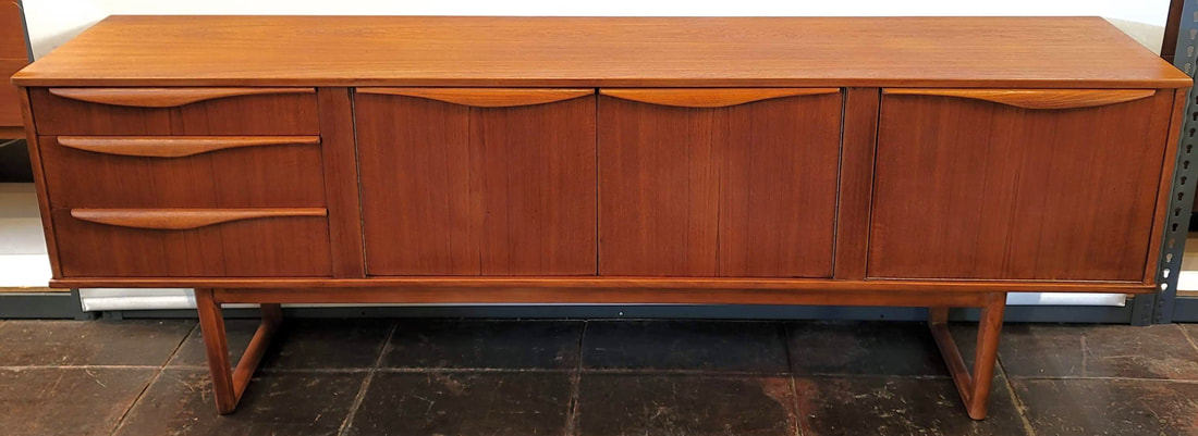 Stonehill Furniture teak sled-leg credenza from their Danish Modern inspired Stateroom Range.  The credenza has three storage drawers on the left with the top drawer lined and containing adjustable spacers for flatware storage.  At center is a double-doored cabinet fitted with one removeable shelf.  The right side features a fall-front light-up cocktail cabinet.  83.5