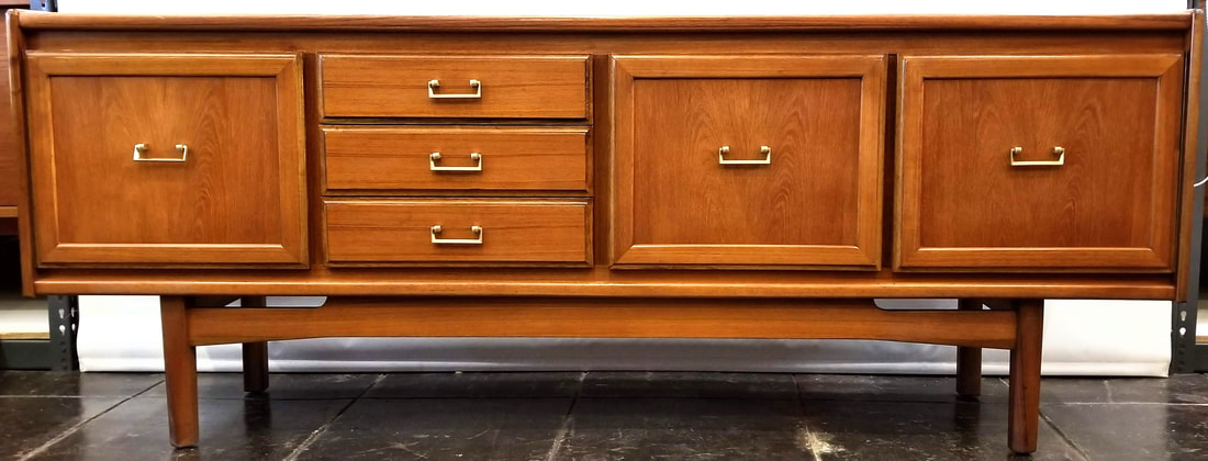 William Lawrence of Nottingham Credenza | England  Mid-1970s design in Southeast Asian crown-cut teak with gold painted brass bail pulls fronting the single door cabinet on the left, the three drawers left of center, and the double-doored storage cabinet on the right.