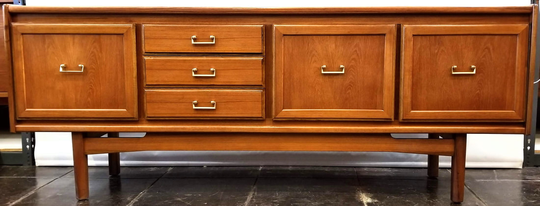 William Lawrence of Nottingham Credenza | England Mid-1970s design in Southeast Asian crown-cut teak with gold painted brass bail pulls fronting the single door cabinet on the left, the three drawers left of center, and the double-doored storage cabinet on the right.